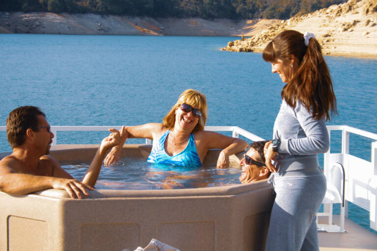 Luxury houseboat anchored near the beautiful sandy shoreline and pine trees at Emerald Cove Marina.