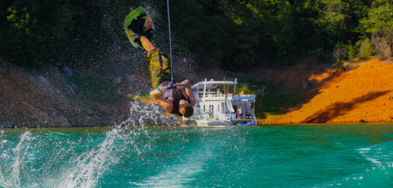 Wakeboarder doing a backflip at bullards bar reservoir with luxury houseboat retal Emerald in the background